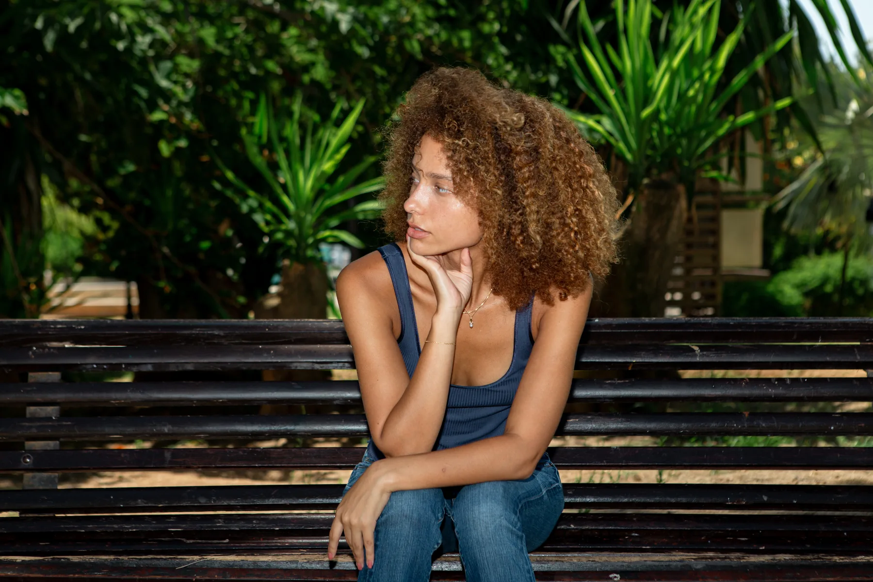 Sophia Coon seated on a park bench, chin resting on her hand, palms behind her